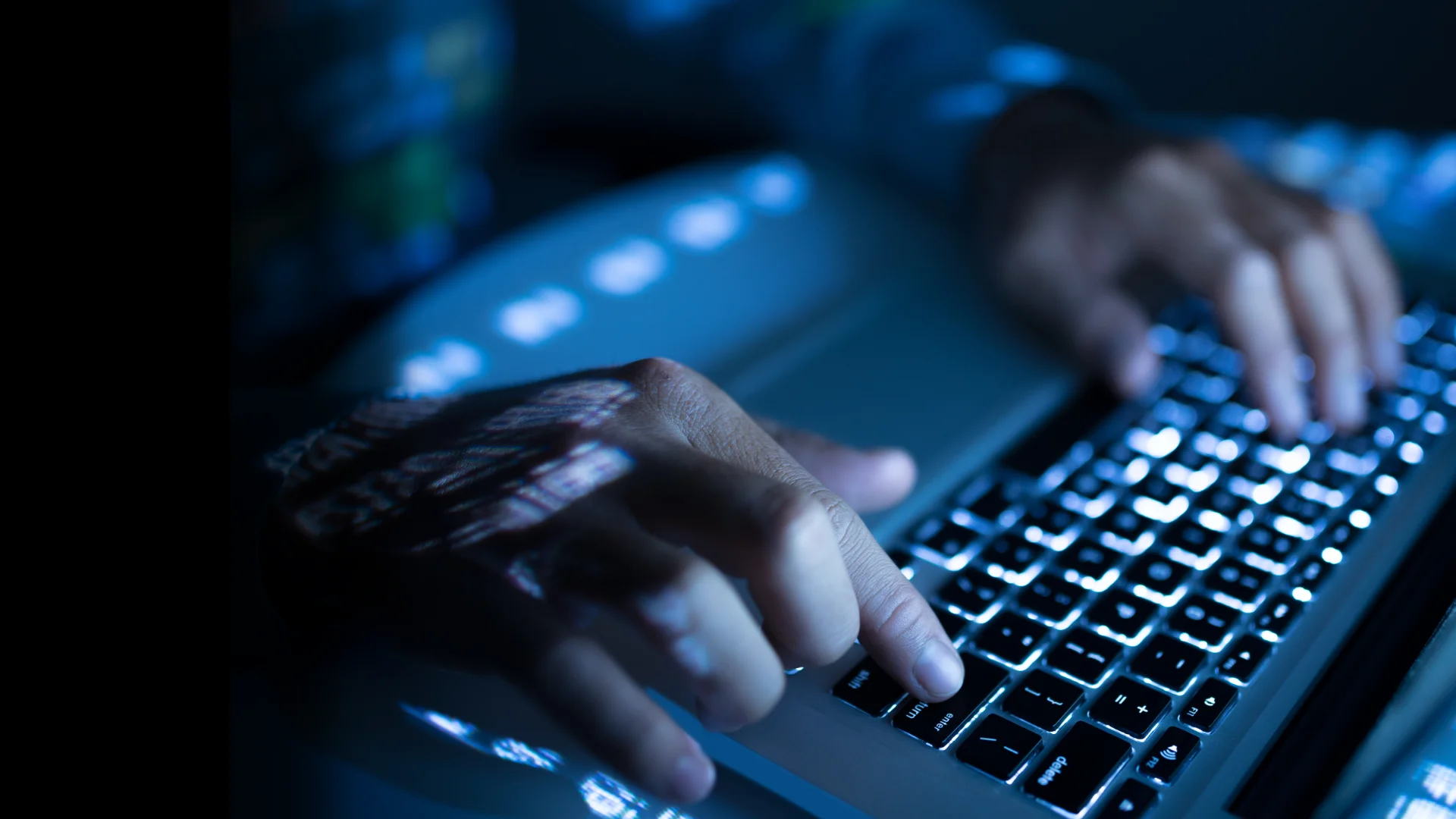 Manos escribiendo en un teclado iluminado
